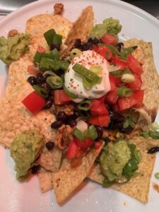 Picture of a plate of nachos topped with ground meat, black beans, corn, tomatoes, guacamole, sour cream and green onions.