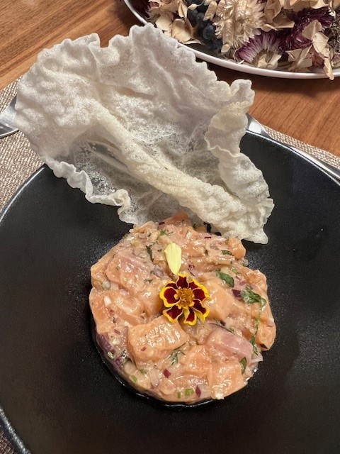 Picture of Salmon Tartare plated with a fried rice paper garnish on a black plate.