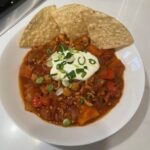 Picture of a bowl of Instant Pot Turkey Chili topped with sour cream and green onions and garnished with tortilla chips.