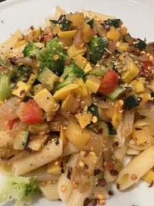 Plate of penne pasta topped with summer vegetables.