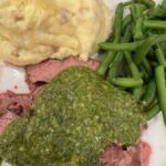 Picture of flank steak on a plate with mashed potatoes, green beans, and chimichurri sauce.