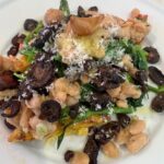 Picture of grilled polenta on a white plate topped with white beans, broccoli rabe, diced tomatoes, garlic, and grilled baby bella mushrooms.