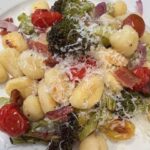 Picture of sheet pan gnocchi on a plate mixed with grilled broccoli, cherry tomatoes, garlic and onion.