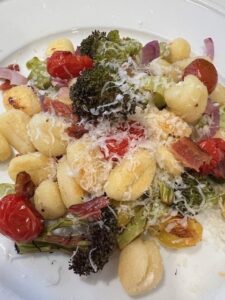 Picture of sheet pan gnocchi on a plate mixed with grilled broccoli, cherry tomatoes, garlic and onion.