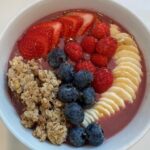 Picture of a simple smoothie bowl topped with fresh strawberries, raspberries, blueberries, sliced banana, and crunchy granola.