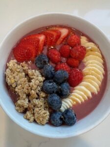 Picture of a simple smoothie bowl topped with fresh strawberries, raspberries, blueberries, sliced banana, and crunchy granola.