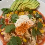 Picture of a bowl of white bean chicken tortilla soup topped with avocado, sour cream, and cilantro.