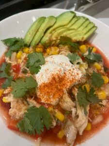 Picture of a bowl of white bean chicken tortilla soup topped with avocado, sour cream, and cilantro.