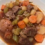 Picture of a bowl of beef stew in a white bowl with potatoes, celery, and carrots.