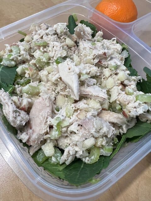 Picture of chicken salad topped on a bed of baby kale in a lunch container.