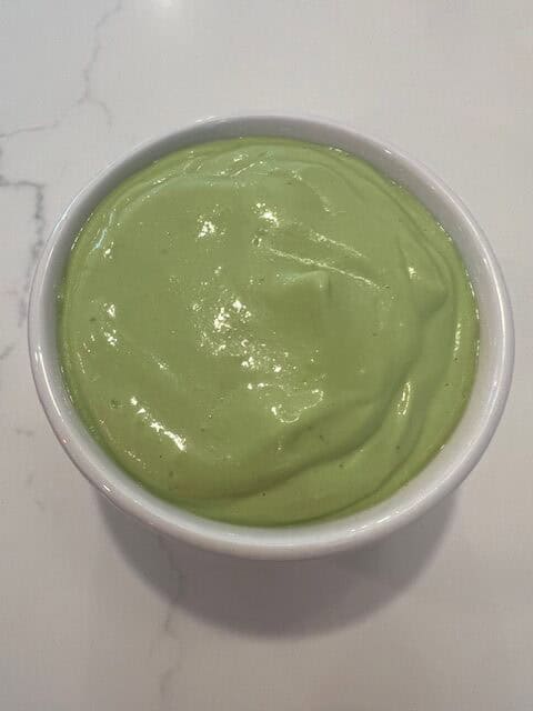 Picture of a white bowl filled with a vibrant lemon basil Greek yogurt dressing.