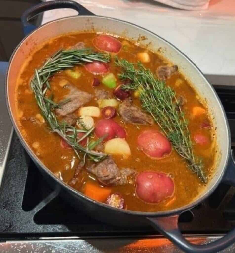 Picture of beef stew cooking on the stove in a pot topped with rosemary.