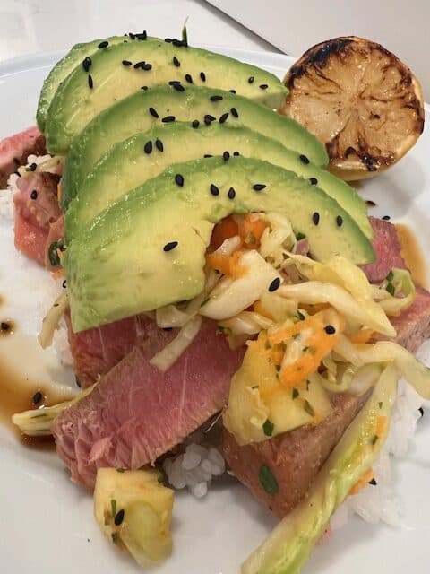 Picture of seared ahi tuna steak on a bed of sushi rice topped with Hawaiian Cabbage Salad and avocados.
