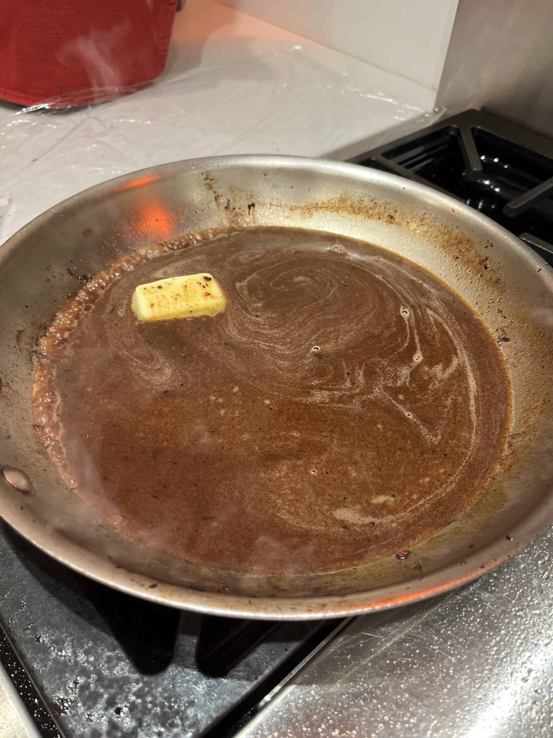 Picture of red wine steak sauce in a skillet pan with butter meting to the side.