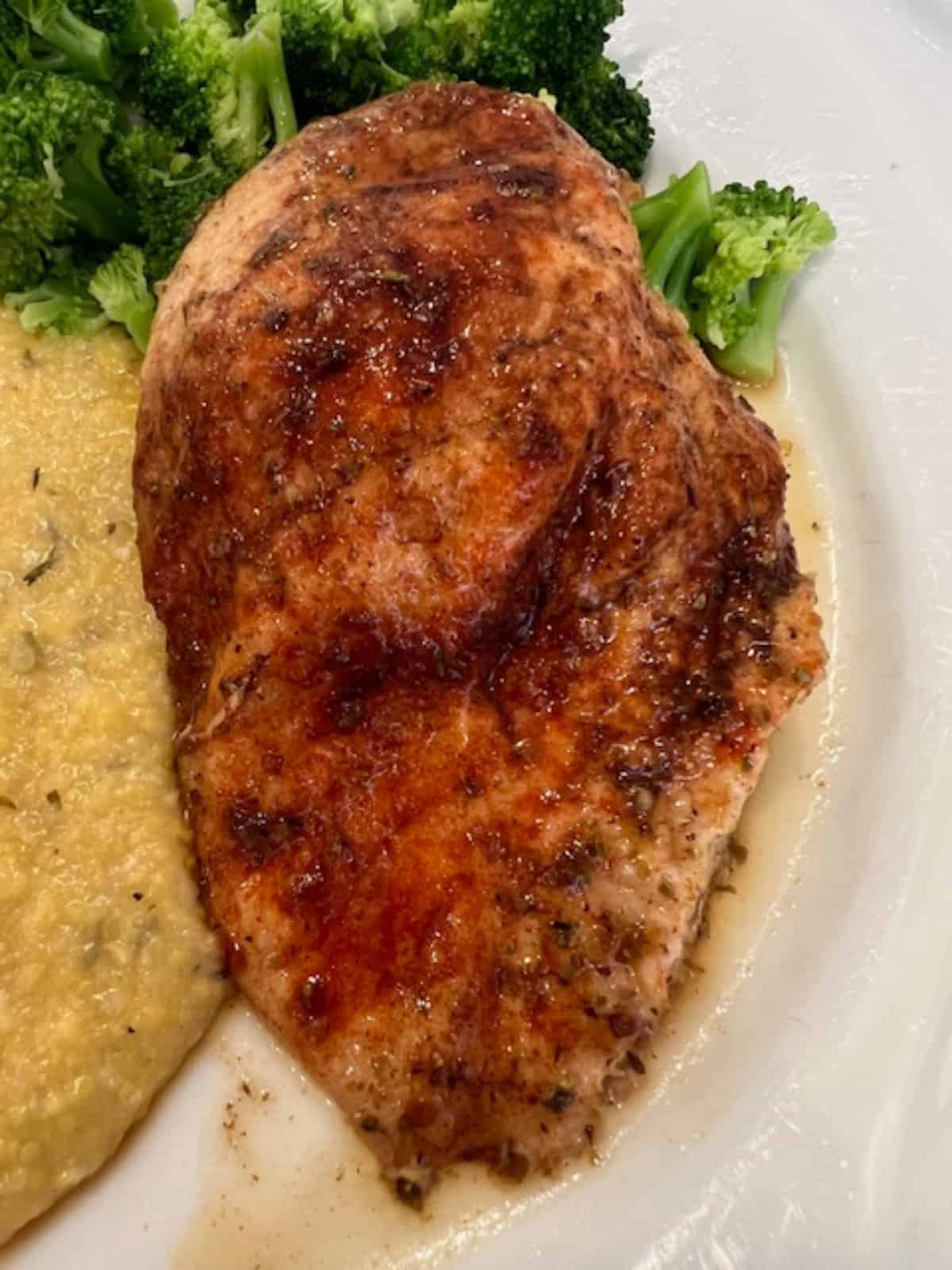 Picture of a Sweet and Savory Baked Chicken Breast on a plate paired with polenta and broccoli.